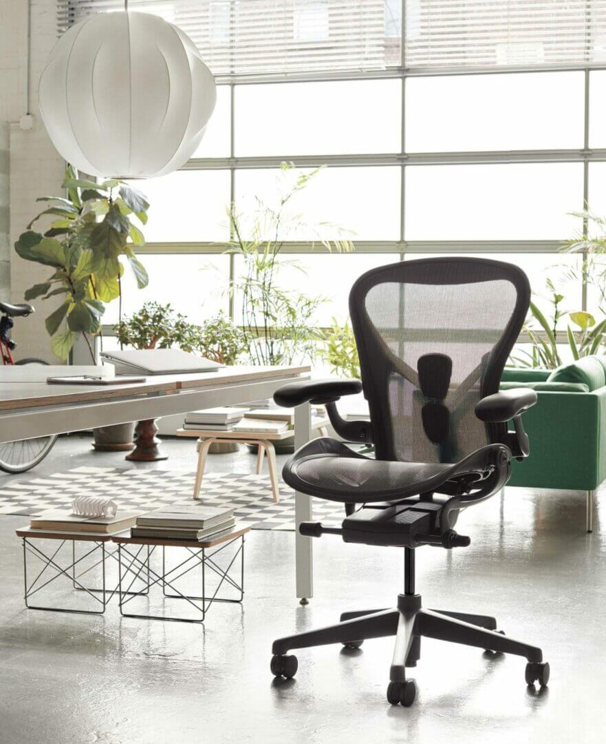 Ergonomic office chair in modern workspace with plants, stylish lighting, and natural light through a large window.