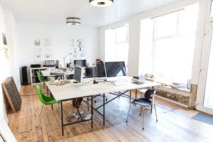 Architect's office with modern desks, chairs, computers, and natural lighting on wood flooring.