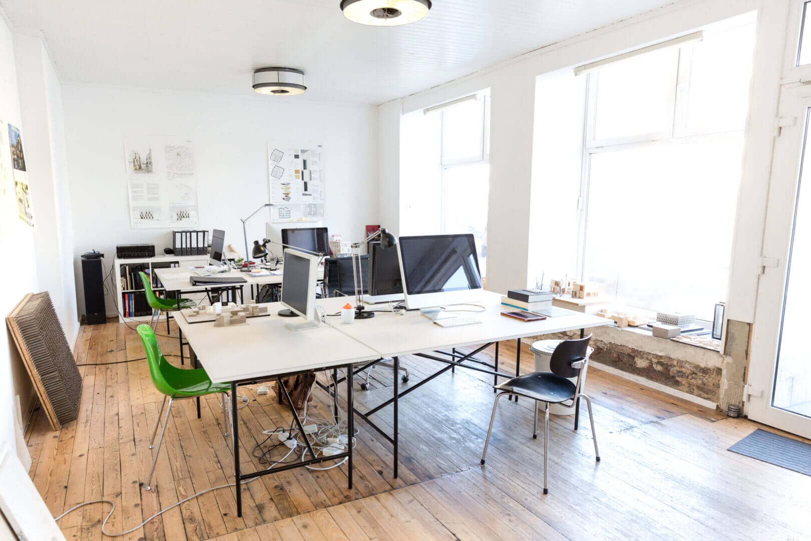Architect's office with modern desks, chairs, computers, and natural lighting on wood flooring.