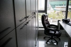 Office space with empty leather chair, desk, and cabinets near large window; modern business environment.